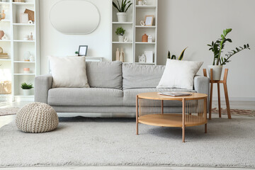 Interior of light living room with grey sofa, table and mirror