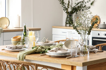 Elegant table setting with beautiful flowers, eucalyptus branches and candles in light kitchen, closeup