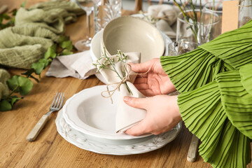 Young woman putting folded napkin with beautiful flowers onto plate on elegantly served table, closeup