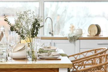 Elegant table setting with beautiful flowers, eucalyptus branches and candles in light kitchen, closeup