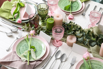 Elegant table setting with beautiful tulip flowers, green leaves and candles in restaurant
