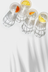 Citrus Infused Water in clear Glasses casting artistic light reflections and palm leaf shadows at sunlight. Summer drink concept, minimal pattern, flavored water with yellow red slices of fruit