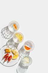 Fruit Infused Water in Glasses and plate with Shadows at sunlight on White background. Aesthetic Top view summer detox drink with slices of lemon and orange with sun flare from glass cups