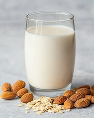 A glass of creamy almond milk surrounded by whole almonds and oats, showcasing a healthy and nutritious beverage option.