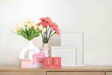 Cube calendar with date of Mother's Day, flowers and blank frames on shelf near light wall
