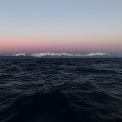 Serene ocean sunrise, distant snow-capped mountains, calm waves, peaceful travel background