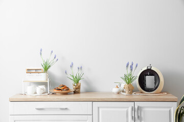 Beautiful Muscari flowers with buns and coffee machine on kitchen counters near light wall
