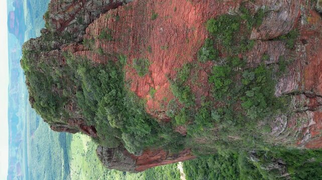Vertical format aerial flyover of rugged summit of red rock pillar