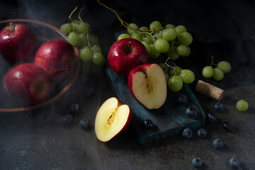 Top view of red apples, green grapes, and blueberries with steam around them on a cutting board