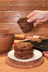 Dipping a tasty chocolate chip handmade cookie into a glass of milk at a wooden table, closeup. Selective focus