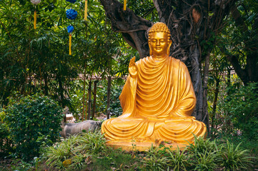Obraz premium Golden Buddha statue surrounded by tropical plants in a garden in Asia.