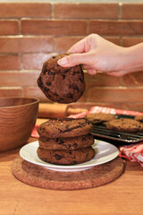 Dipping a tasty chocolate chip handmade cookie into a glass of milk at a wooden table, closeup. Selective focus