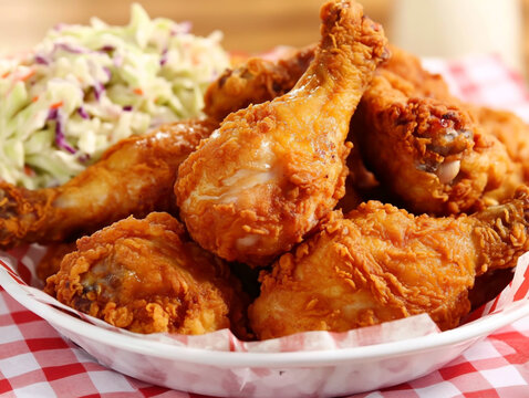 A basket of golden-brown fried chicken drumsticks, accompanied by the classic coleslaw - Powered by Adobe
