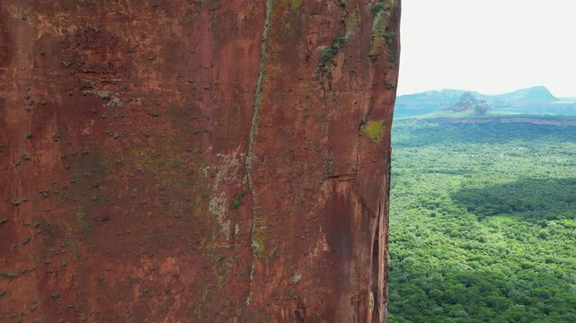 Overhanging steep sandstone rock cliff high above lush green forest