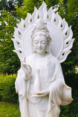 Fototapeta premium White Buddha statue surrounded by tropical plants in a garden in Asia.