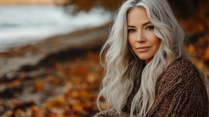 Naklejka premium Elegant woman with long grey hair smiles in a cozy brown sweater. Use it for articles about style, autumn, or positive aging concepts.