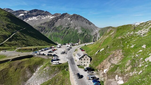 Flight over parking lot at top of mountain pass Furka Pass with serpentine road towards mountain Finsteraarhorn panorama in the Swiss Alps, Switzerland
