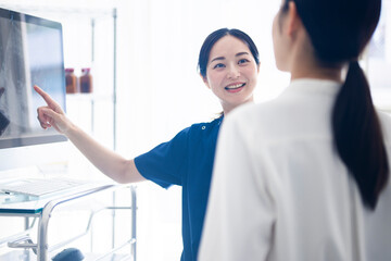 A female doctor in blue scrubs is smiling and pointing at a medical monitor while explaining...