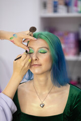 Fototapeta premium woman with green hair is getting her eyes done by a stylist. The stylist is using a brush to apply makeup to the woman's eyes. The woman is relaxed and comfortable with the process