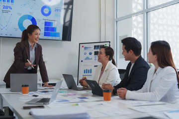 Asian businesswoman leading a meeting with her team, discussing marketing strategy and analyzing financial data displayed on a large screen and whiteboard in a modern office setting