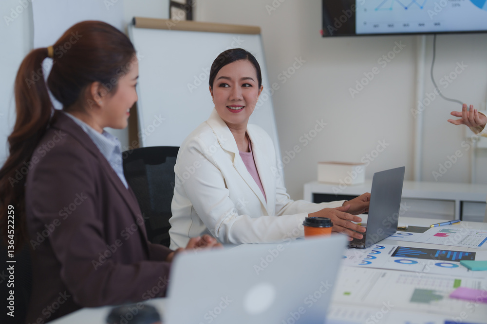 Poster two businesswomen are interacting during a corporate meeting, utilizing a laptop and reviewing print