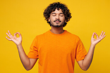 Young spiritual Indian man wear orange t-shirt casual clothes hold spreading hands in yoga om aum...
