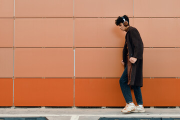 Stylish man in a coat and jeans walks past a wall with orange and brown tiles