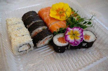 Mix of sushi rolls with salmon, avocado, smoked eel, in a plastic food delivery box.