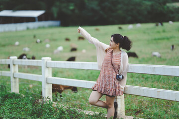 Naklejka premium A woman stands by a fence in a field, pointing towards grazing animals, capturing a moment of joy and connection with nature.