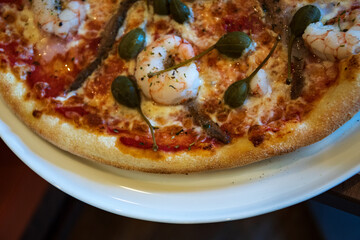 Delicious pizza with shrimps, anchois, capers and mozzarella buffalo served on plate. Traditional Italian cuisine. Simple gourmet lifestyle.
