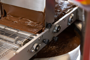 Liquid chocolate flows smoothly along a conveyor belt in a factory.