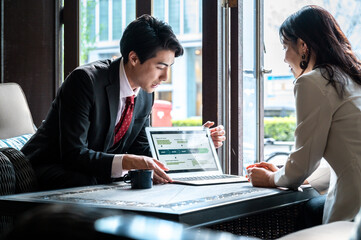 A businessman presents a digital strategy on his laptop to a female colleague in a bright café....