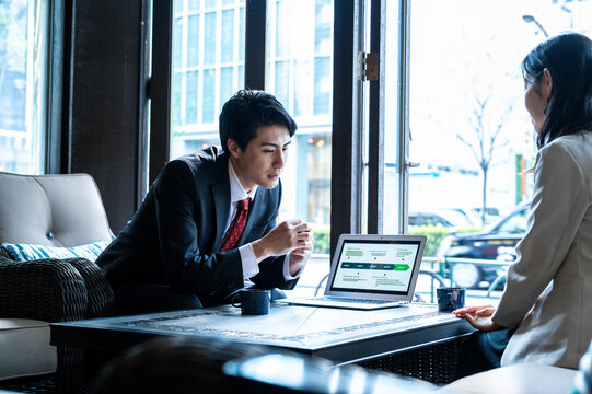 A businessman presents a digital strategy on his laptop to a female colleague in a bright café. They both appear focused, exchanging ideas during the meeting.