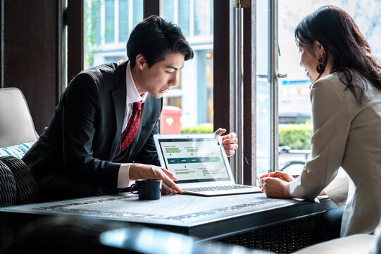 A businessman presents a digital strategy on his laptop to a female colleague in a bright café. They both appear focused, exchanging ideas during the meeting.