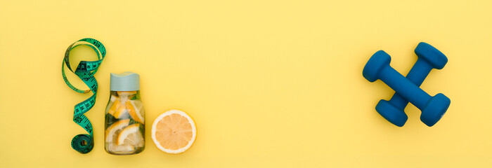 orange, water bottle, tape measure, dumbbells on yellow background flat lay