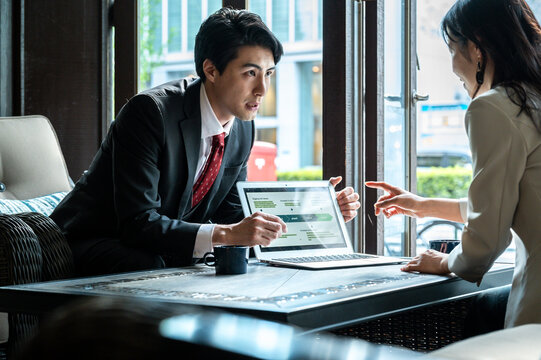 A businessman presents a digital strategy on his laptop to a female colleague in a bright café. They both appear focused, exchanging ideas during the meeting.
