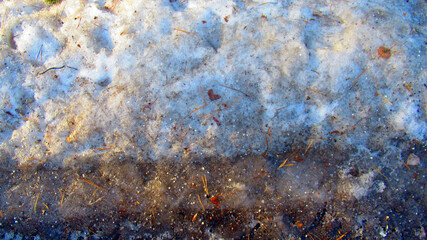 Dirty snow illuminated by the sun. Autumn fallen leaves and reagents on snow