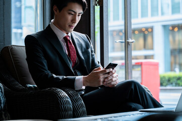 A cropped view showing a businessman using a smartphone with both hands, seated in a café. The composition emphasizes connectivity and mobile productivity.