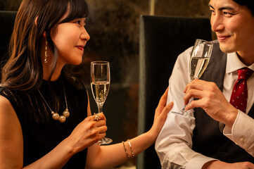 A woman in a sleeveless black dress smiles while holding a champagne glass at an upscale bar. The warm lighting and her elegant accessories convey a festive, celebratory mood.
Keywords: