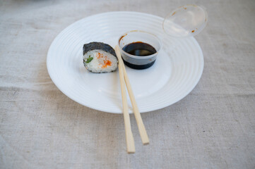 sushi roll with chopsticks and wasabi sauce in a plastic container on a white plate.