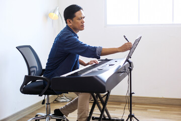 Millennial Musician Guy In Casual Style Writing On Sheet Music While Playing Piano Keyboard