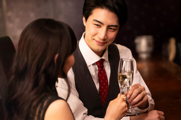 Stylish man in formal attire looking at his partner while toasting champagne in a moody upscale bar. The scene captures romantic eye contact and elegant intimacy.