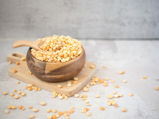 A pile of dried yellow split peas in a wooden bowl on a concrete background