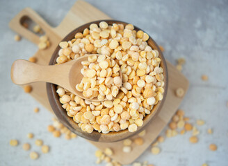 A pile of dried yellow split peas in a wooden bowl on a concrete background