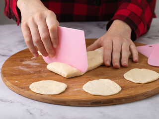 Close-up view of child's hands cutting dough into pieces on wooden cutting board using pink plastic...
