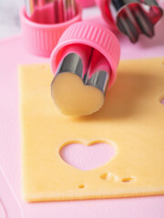 Figured stamp knife with heart cut out of cheese piece on table, close-up