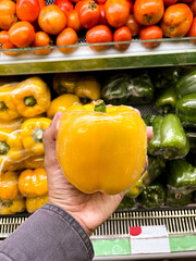 hand holding yellow bell pepper or paprika on groceries market
