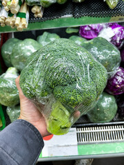 hand holding fresh broccoli wrapped in plastic at groceries store