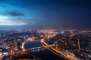 Cityscape from the height of an airplane flight at night. Illuminated streets, buildings, bridges, embankment