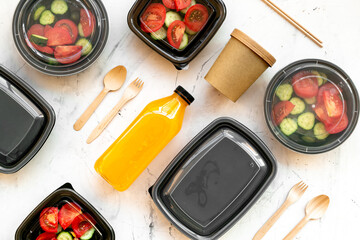 Tomatoes salad in lunch boxes with orange juice in a bottle and disposable cutlery, top view